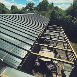 A building's roof with a metal roof and a wooden deck area with chairs and a table.