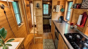 A compact kitchen with wooden walls, a stove, a sink, and a small dining area with a table and chair.
