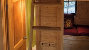 A wooden cabin with a loft bedroom, a ladder to the lower bunk, and a window with a view.
