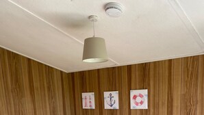 A room with a wooden panel wall, a brown sofa with red cushions, a small wooden table, and a ceiling light fixture.