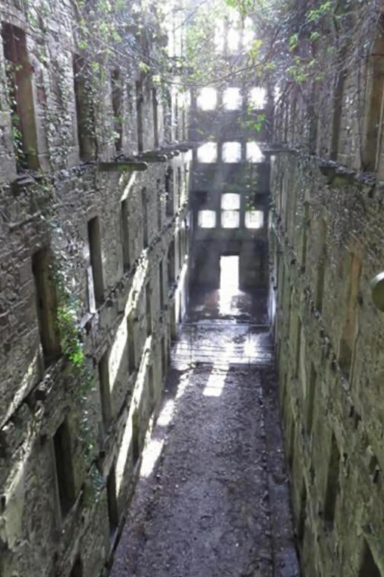 A narrow, stone corridor with arched openings and a rough, uneven floor.