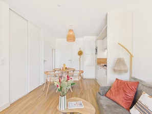 Un espace de vie moderne comprenant un coin repas, une kitchenette et un canapé agrémenté d’un coussin décoratif.