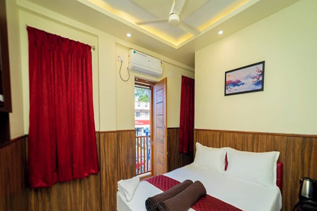 A hotel room with a bed, a ceiling fan, an air conditioning unit, and a painting on the wall.
