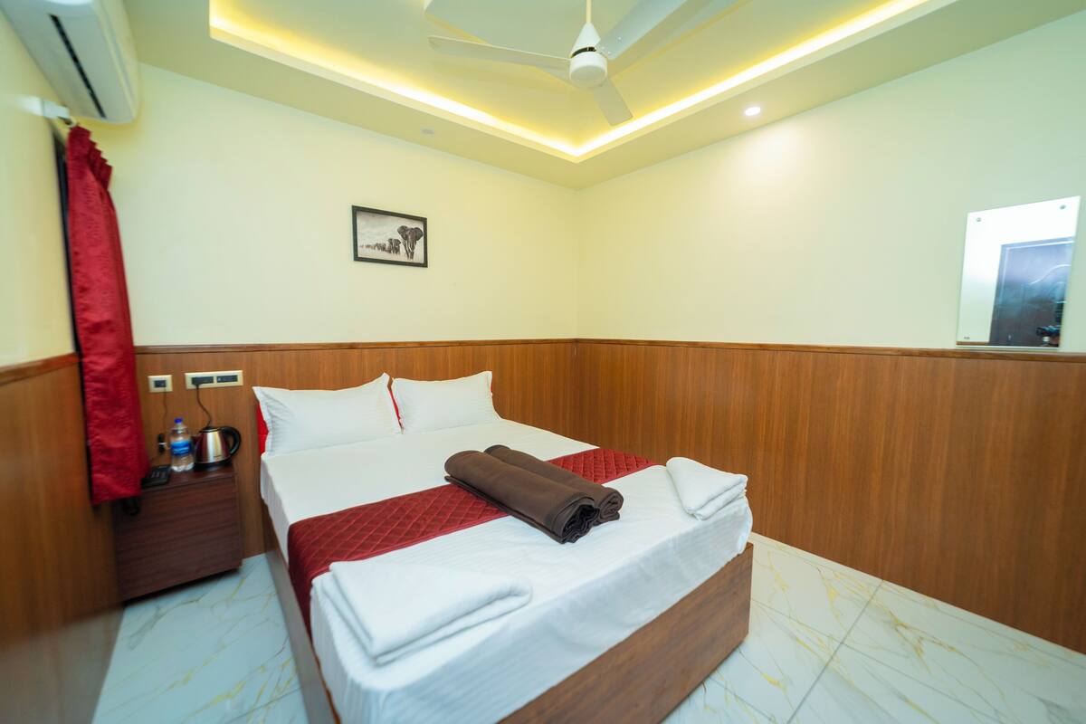 A hotel room with a bed, a nightstand, a red curtain, a ceiling fan, and a framed picture on the wall.