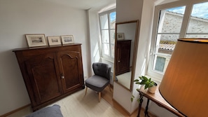 A room with a wooden wardrobe, a grey armchair, a mirror, and a window with a view of a building. - Lake view 3-level 35m2 Apartment in Riex -Cully (Bourg-en-Lavaux)