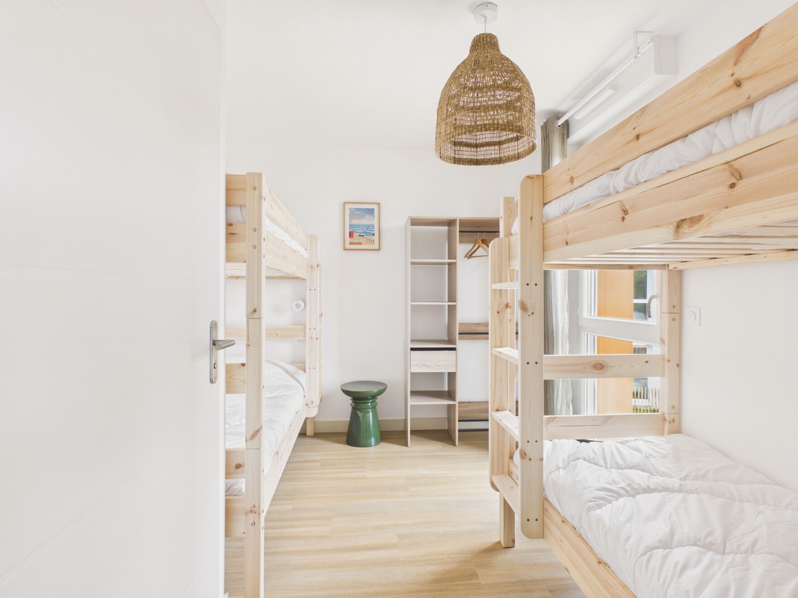 Een slaapkamer met stapelbed, een hanglamp, een groene kruk en een inbouwkast met planken.