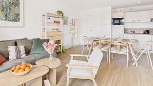 Un salon moderne comprenant un canapé, une table à manger avec des chaises, un coin cuisine et un luminaire suspendu.