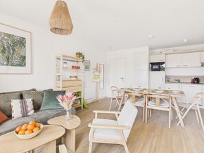 A modern living room with a sofa, a dining table with chairs, a kitchen area, and a hanging light fixture. - The Snap - 6 guests - shared pool (Biscarrosse)