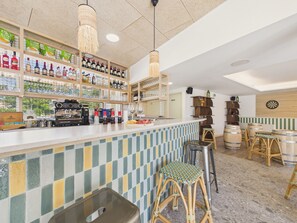 Eine Bar mit Regalen voller Spirituosenflaschen, einer Kaffeemaschine, Barhocker und einem Dartspiel.