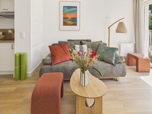 A modern living room with a striped sofa, a wooden side table with a vase, and a bench. - The Board -apartment 4 ad 1 kid -shared swimming pool (Biscarrosse)