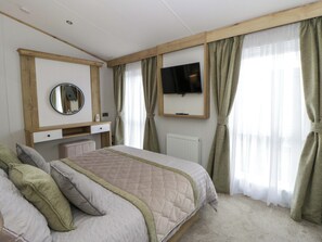 A bedroom with a bed, a bedside table, a mirror, a television, and curtains. - The Dorchester at Bay View (New Quay)