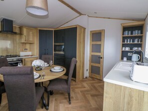 A modern kitchen with wooden cabinets, a dining table set for four, and a built-in oven. - The Dorchester at Bay View (New Quay)