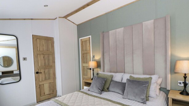 A bedroom with a bed, bedside tables, a mirror, and a door. - The Dorchester at Bay View (New Quay)