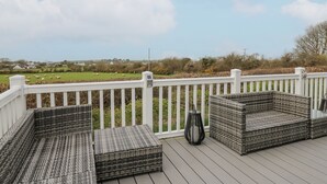 A deck with wicker furniture and a white railing overlooking a green landscape. - The Dorchester at Bay View (New Quay)