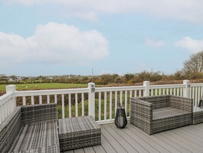 A deck with wicker furniture and a white railing overlooking a green landscape. - The Dorchester at Bay View (New Quay)