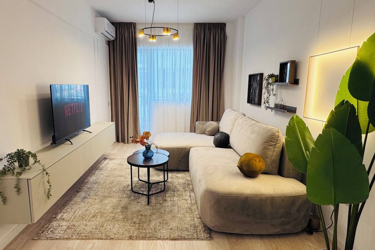 A modern living room with a flat-screen TV, a sofa, a coffee table, and a large plant.