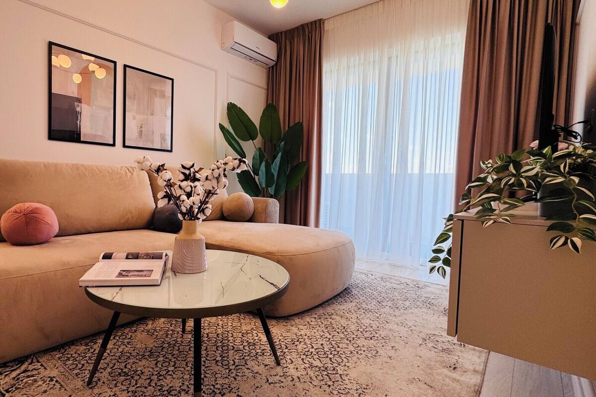 A modern living room with a beige sofa, a round coffee table, and a large plant.
