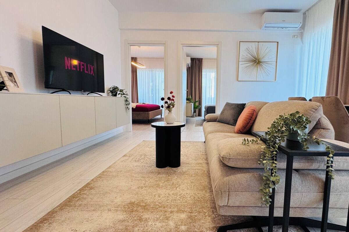 A modern living room with a sofa, a coffee table, a TV mounted on the wall, and a plant on the side table.