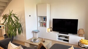 Een moderne woonkamer met een zithoek, een flatscreen televisie, een trap en een potplant.