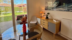 Een moderne woonkamer met een glazen tafel, een bank, een bureau met een lamp en een groot schilderij van een golf.