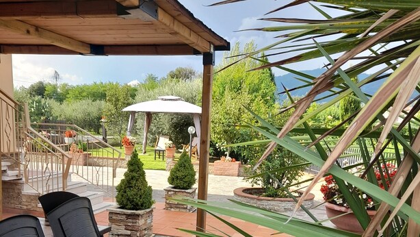 A covered patio area with stone flooring, outdoor seating, and potted plants. - 10 minutes from Lucca, 130 sq. m. apartment with garden, pets dom. allowed (Capannori)
