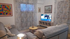 A living room with a sofa, a TV, a lamp, and floral curtains. - 10 minutes from Lucca, 130 sq. m. apartment with garden, pets dom. allowed (Capannori)