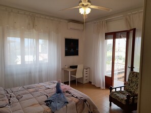 Ett sovrum med en säng, ett skrivbord, en stol, en takfläkt och en balkong.