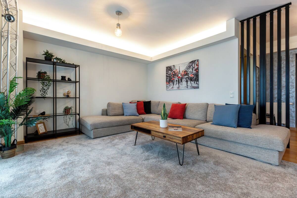 A living room with a sectional sofa, a wooden coffee table, a bookshelf, and a painting on the wall.