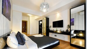 A modern bedroom with a large bed, a TV, a mirror, and a chandelier. - Great Apartments in Prime North Location (Bucharest)