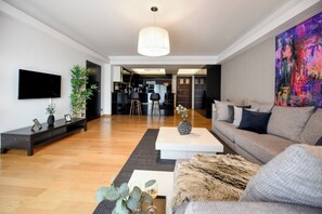 A modern living room with a sofa, coffee table, and a TV. There is a kitchen in the background. - Great Apartments in Prime North Location (Bucharest)