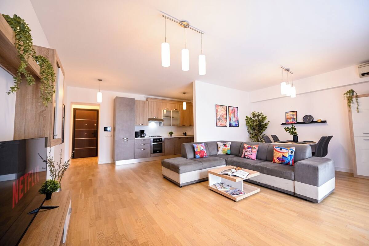 A modern living room with a grey sectional sofa, wooden flooring, and pendant lighting.
