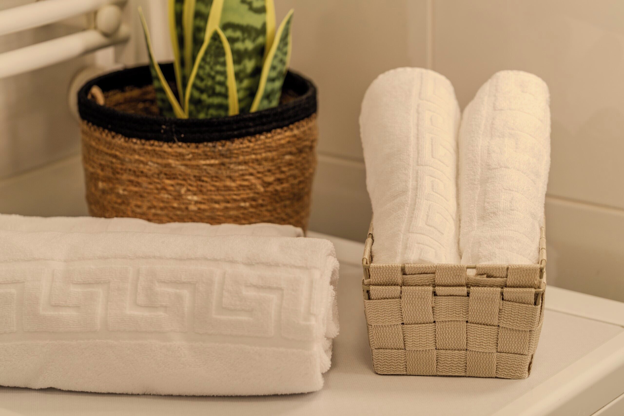 Un baño con una toalla blanca, una toalla color beige y una cesta de mimbre con toallas.