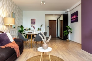Una sala moderna con un sofá, una mesa de comedor con sillas, una mesa de centro con un florero y una zona de cocina al fondo.