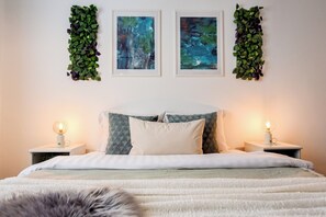 Un dormitorio con una cama, dos mesitas de noche, una lámpara y dos obras de arte enmarcadas en la pared.