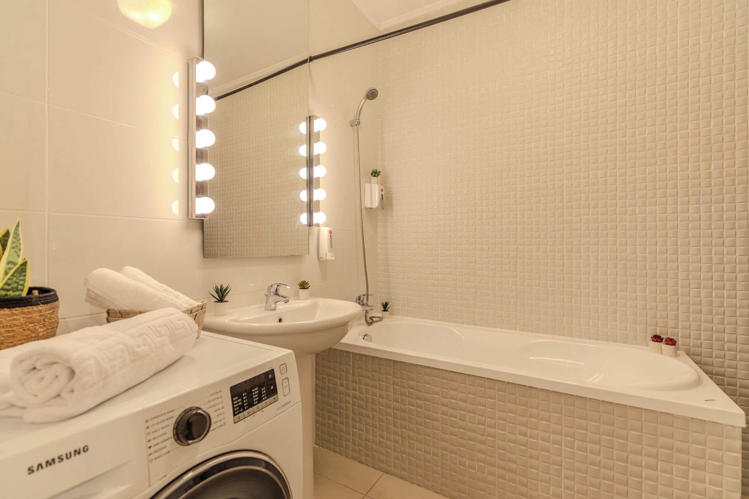 Une salle de bain équipée d’un lave-linge, d’un évier, d’une baignoire et d’un miroir avec éclairage.
