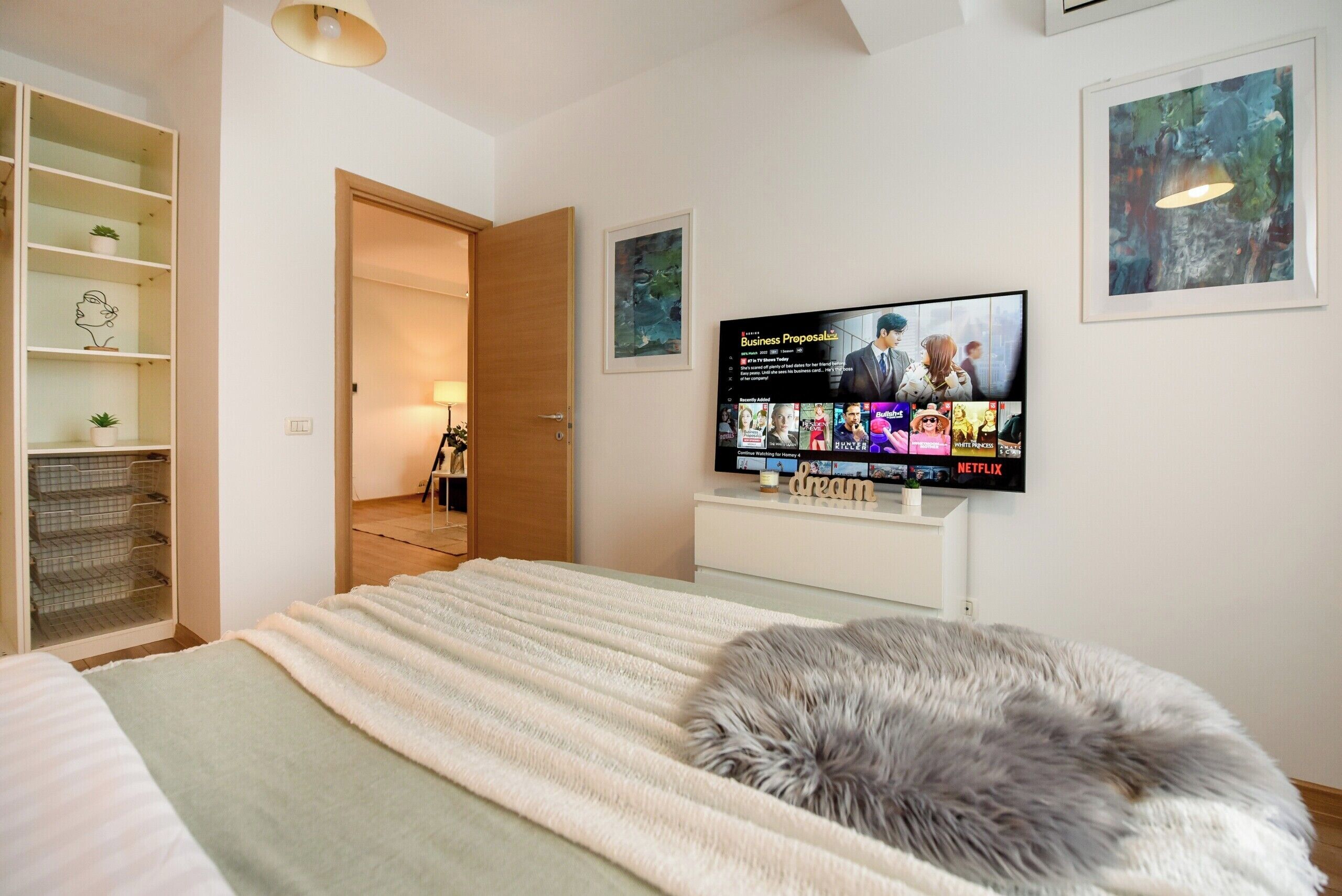 A bedroom with a bed, a TV displaying a movie, a wardrobe, and a door leading to another room.