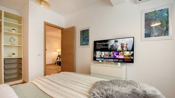 A bedroom with a bed, a TV displaying a movie, a wardrobe, and a door leading to another room.