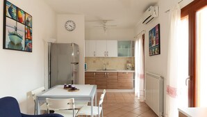 Cocina compacta con armarios blancos, un refrigerador, una mesa de comedor con sillas y un ventilador de techo.