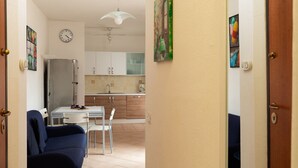 Una habitación con sofá, mesa de comedor, sillas, refrigerador, reloj y ventilador de techo.