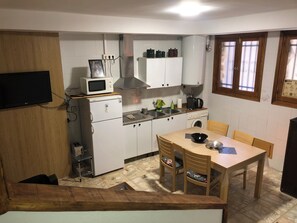 Cocina compacta con microondas, estufa y lavabo. Hay una mesa de comedor con sillas y un ventanal pequeño.