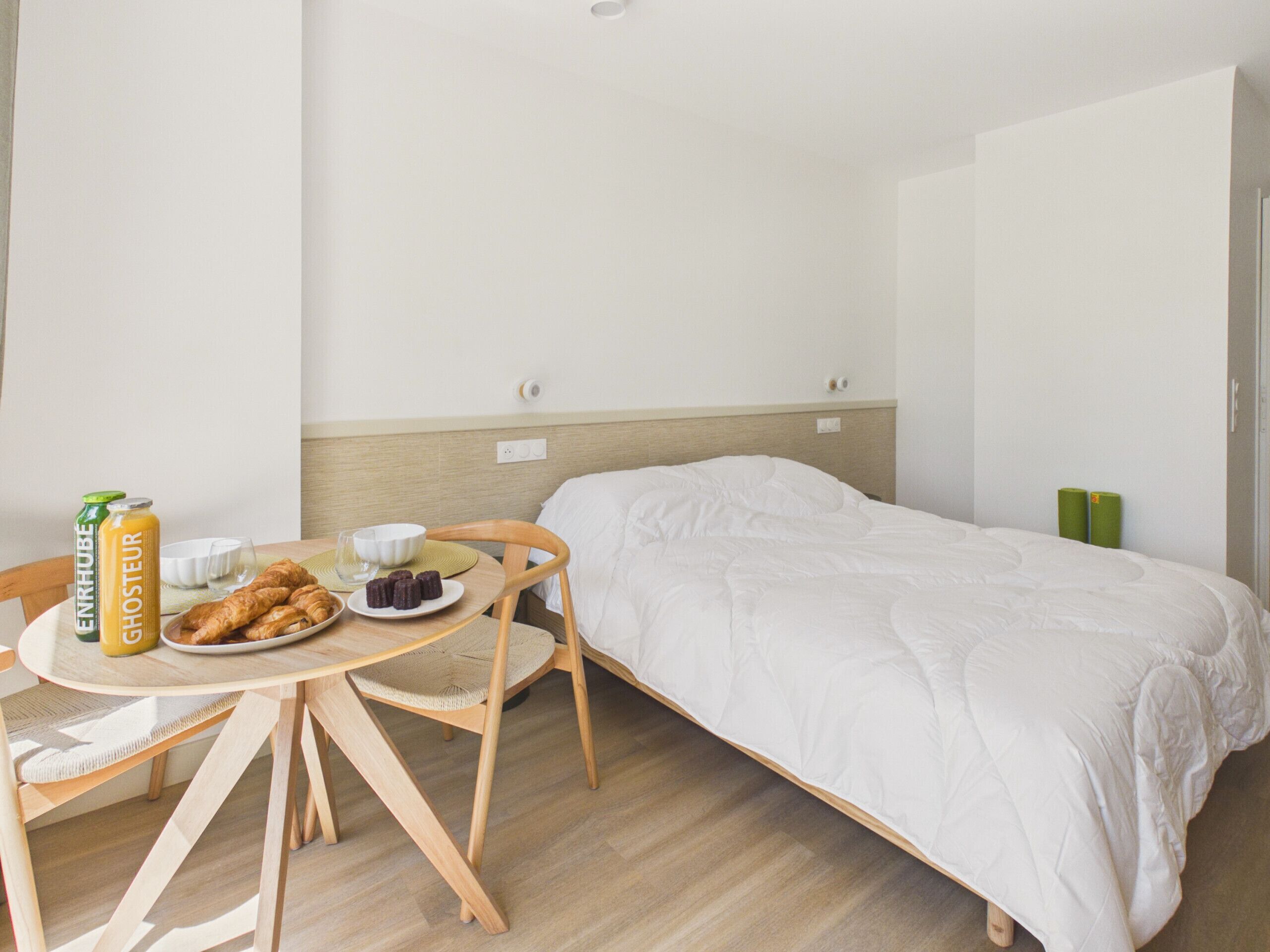 Hotellihuone, jossa on sänky, puinen pöytä, jonka päällä on aamiaisruokia, ja vihreä seinä.