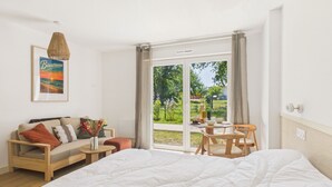 Ein Schlafzimmer mit einem großen Bett, einer Couch, einem Esstisch und Blick ins Freie.