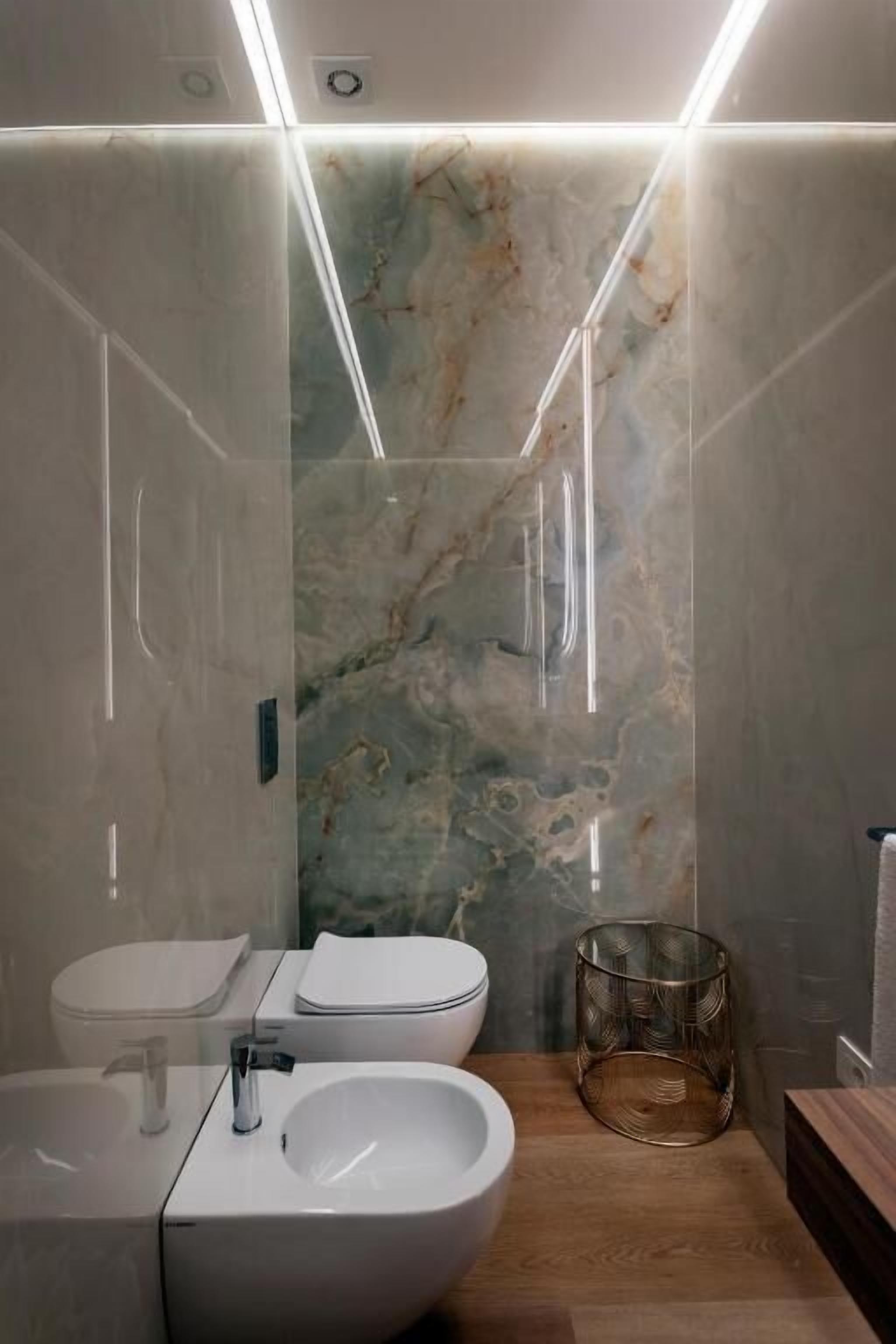 Un bagno moderno con una parete in marmo, un bidet, un lavandino e un contenitore di vetro.