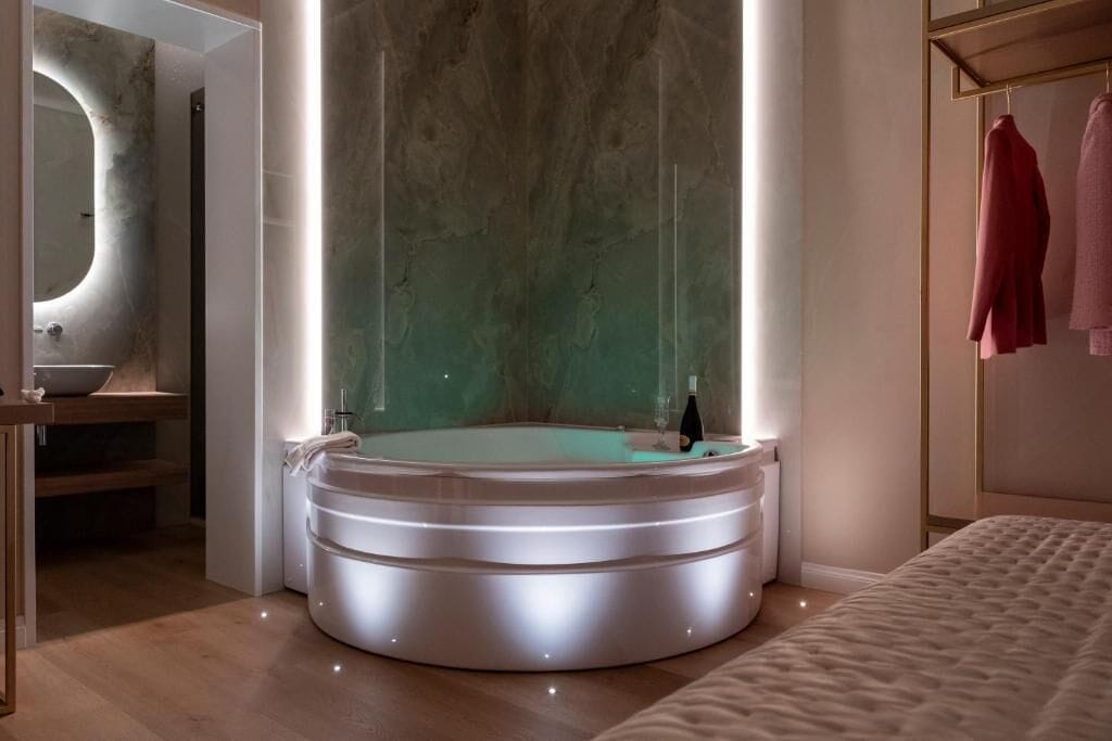 Un baño moderno con una bañera independiente, un tocador con espejo y una cama con cabecero.