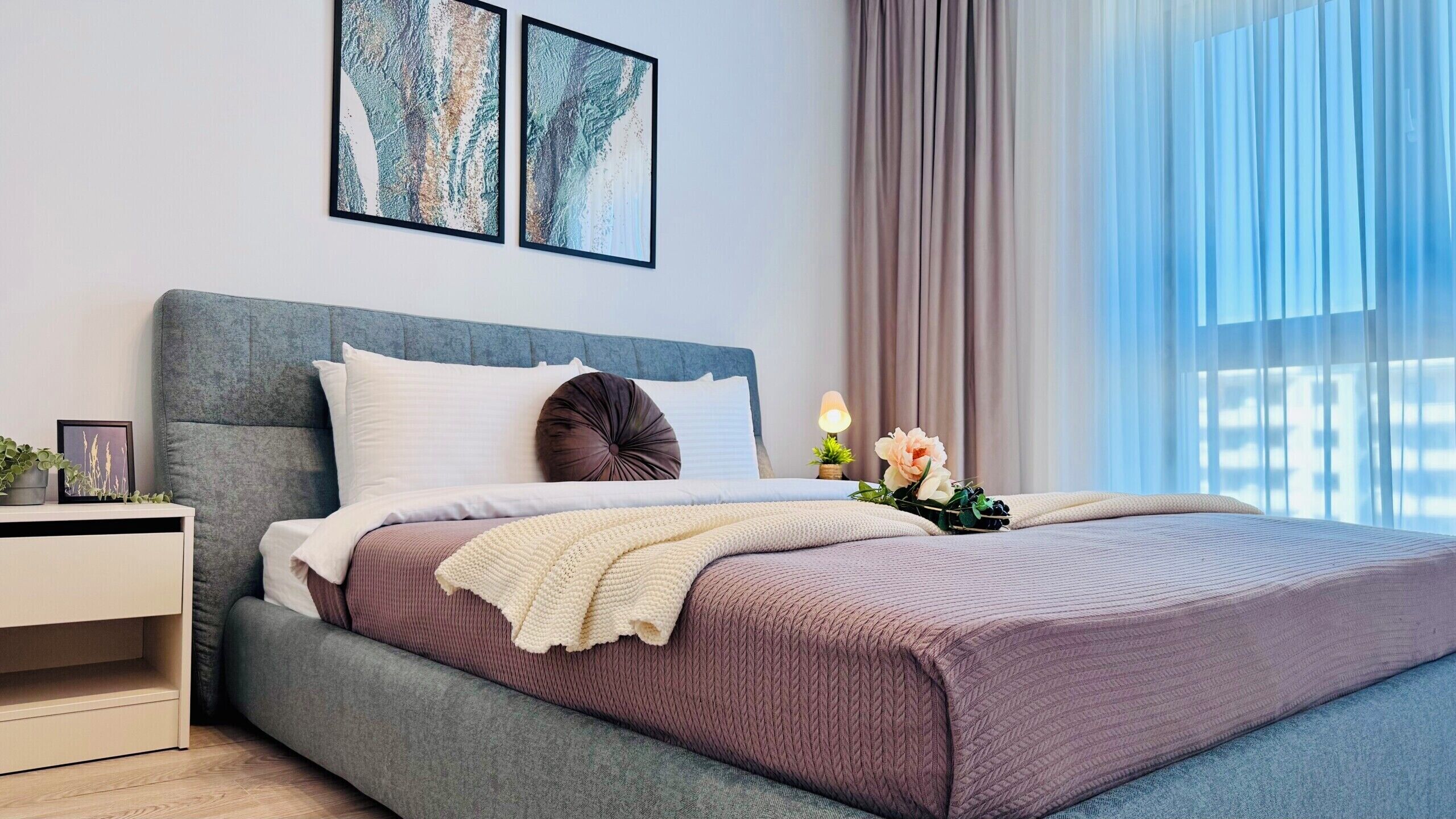 A modern bedroom with a bed, bedside table, and a window with curtains.