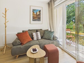 A modern living room with a sofa, a wooden coat rack, a framed picture on the wall, and a view through a glass door. - La Planche Malibu - apartment for 4- shared pool (Biscarrosse)