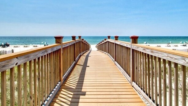 Una passerella di legno che conduce a una spiaggia con ombrelloni e lettini.