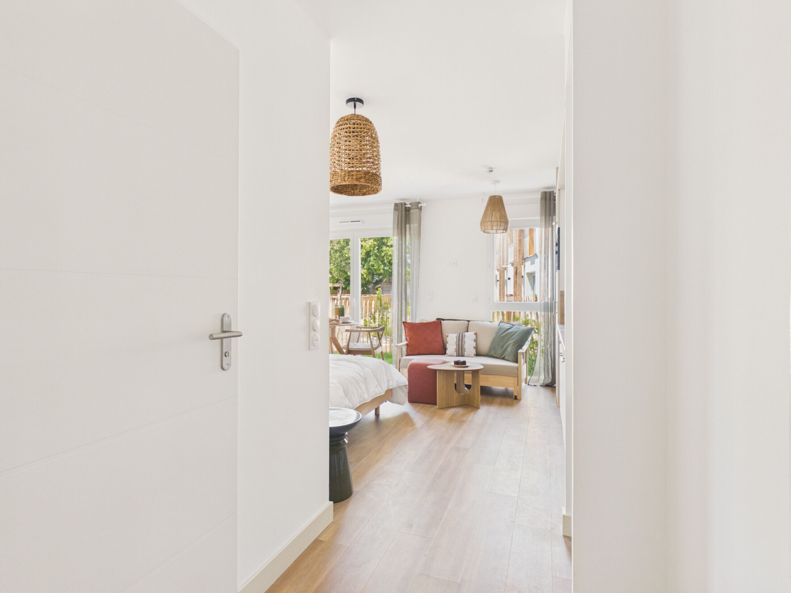 A modern interior with a wooden floor, a sofa with cushions, a small round table, and a hanging light fixture.