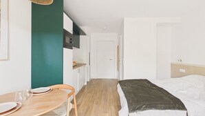 A compact hotel room with a bed, a small kitchenette, a dining area with a table and chairs, and a hanging light fixture. - Le Funboard - studio for 3 - shared pool (Biscarrosse)