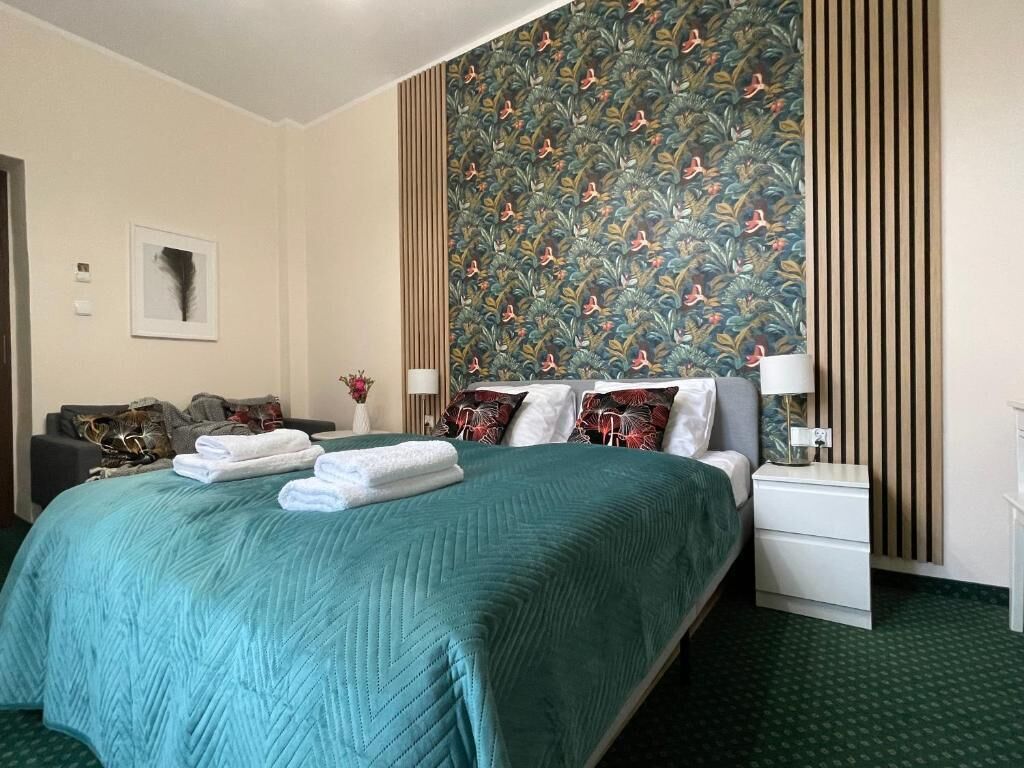 Et hotelværelse med en stor seng, et natbord, en lampe, en væg med blomstermønster og et billede i ramme på væggen.